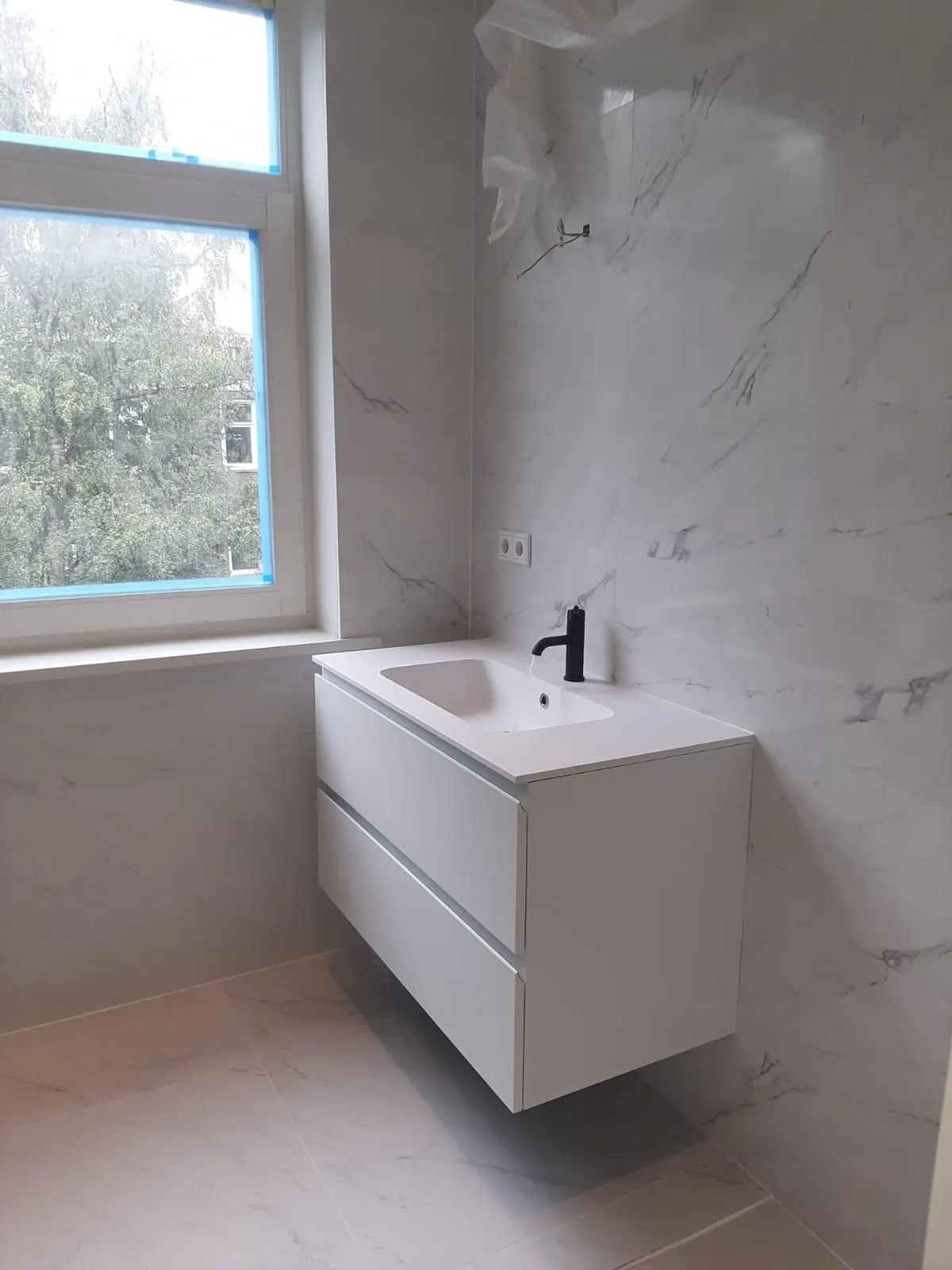 Floating vanity unit with black tap against marble wall tiles, bathroom renovation by Klussen Fixer